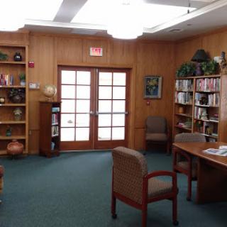 A cozy library space featuring wooden walls, bookshelves filled with books, and comfortable chairs.