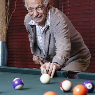 An elderly man playing pool on a billiards table indoors.