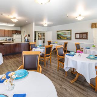 A well-lit dining area with set tables and chairs adjacent to a kitchen.