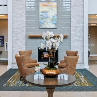A modern lobby features a cozy seating area with four chairs around a table adorned with orchids, set against a backdrop of a fireplace and artwork.