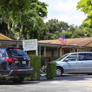 A view of a building with parked cars and an American flag in front.