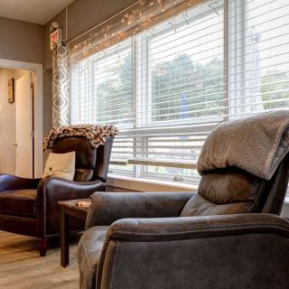 A cozy living room with comfortable chairs and large windows with blinds.