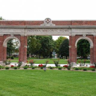 A historical brick archway entrance with landscaped gardens in a park setting.