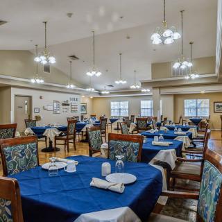 A spacious dining room with neatly set tables featuring blue tablecloths and elegant lighting.