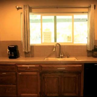 A kitchen with wooden cabinets and a countertop featuring a sink, coffee maker, and a window with curtains.