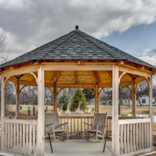 A wooden gazebo with seating in a park setting under a cloudy sky.