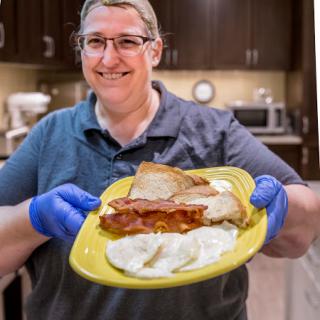 A cheerful person proudly displaying a delicious meal in a kitchen setting.