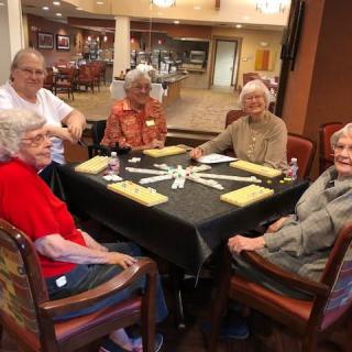 A group of seniors seated around a dining table in a communal setting.