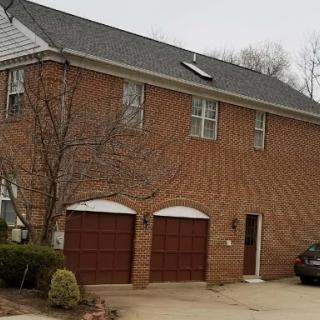 A two-story brick house featuring a garage with two doors and surrounded by trees.