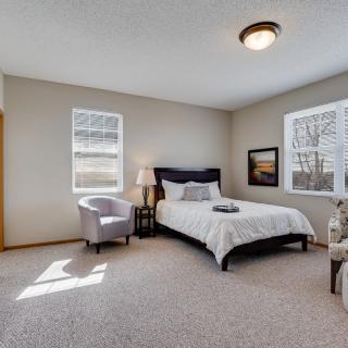 A cozy bedroom with a neatly made bed, armchairs, and warm lighting.