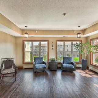 A bright living room with large windows, featuring two blue chairs, a small table, and plants.