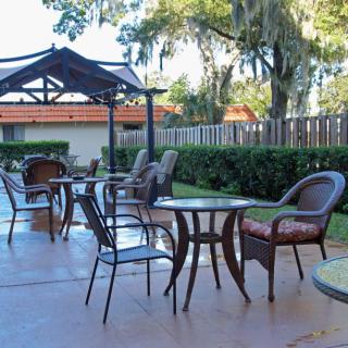 A sunny outdoor patio with tables and chairs set up under a gazebo, surrounded by trees.