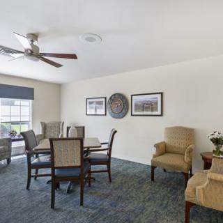 A well-decorated living and dining area featuring a round table with chairs, comfortable armchairs, and a ceiling fan.