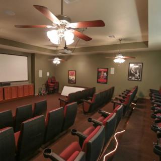 A cozy home theater room with multiple seating rows, ceiling fans, and a projector screen surrounded by movie posters.