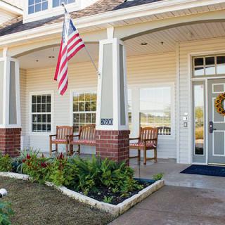 A welcoming front porch with an American flag, garden, and patio furniture.