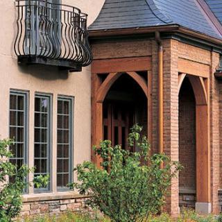 A beautifully designed house facade featuring large windows, a small decorative balcony, and wooden beam details.