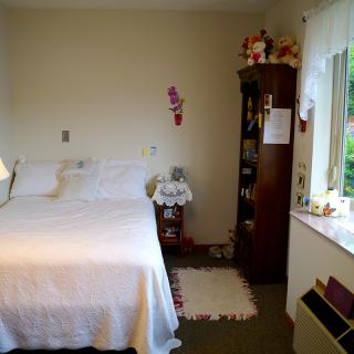 A cozy bedroom with a neatly made bed, a bookshelf, and sunlight streaming through the window.