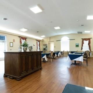 A spacious dining room with wooden flooring, featuring tables and chairs neatly arranged under bright lighting.