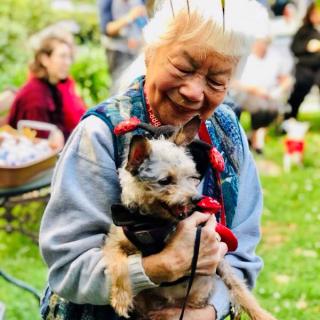 An elderly woman joyfully holding her dog in a park setting.