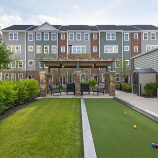 A residential apartment complex featuring a landscaped backyard with a bocce court and outdoor seating area.