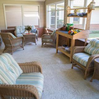 A bright and inviting sunroom with cozy wicker furniture and lush green plants.