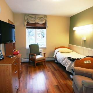 A cozy and minimalist bedroom with a hospital bed, wooden floors, and a television.