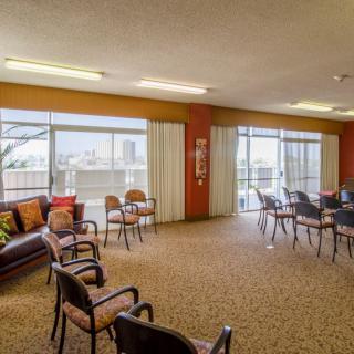 A spacious community room with multiple chairs arranged in a circular formation, featuring large windows that allow natural light to fill the space.