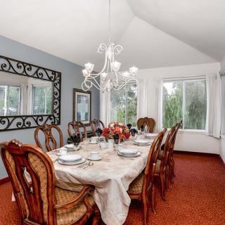 An elegantly set dining room featuring a large dining table with upholstered chairs, accented by a chandelier and a decorative mirror on the wall.