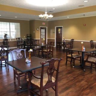 An empty dining room with wooden tables and chairs, featuring a chandelier and wooden flooring.