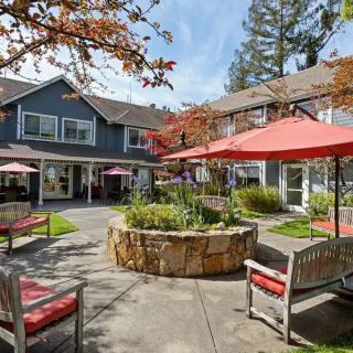 A peaceful courtyard featuring benches and umbrellas surrounded by a garden and building.