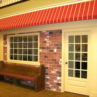 A quaint storefront featuring a red awning, brick facade, and a wooden bench by the glass door.