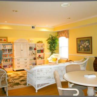 A cozy living room with bright yellow walls, featuring a comfortable seating area and a well-stocked bookshelf.