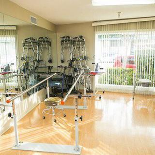 A well-lit rehabilitation room with exercise equipment and parallel bars for physical therapy.