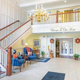 A welcoming lobby with elegant decor, featuring a staircase, chandelier, and comfortable seating.