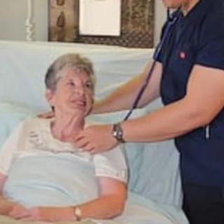 A doctor uses a stethoscope to examine an elderly patient in a hospital bed.