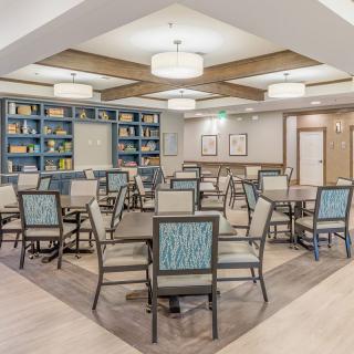 A modern dining area with multiple tables and chairs, surrounded by bookshelves and illuminated by stylish ceiling lights.