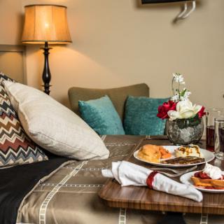 A cozy living room setup featuring a breakfast tray on a side table, adorned with decorative pillows and a lamp for ambiance.