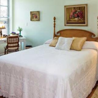 A cozy and well-decorated bedroom featuring a comfortable bed, art on the walls, and a quaint workspace near the window.