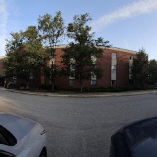 A view of a brick apartment building surrounded by trees with parked cars on the street.