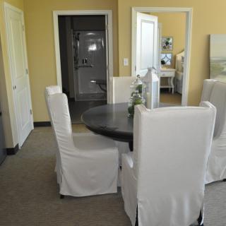 A modern dining room with a dark round table and white upholstered chairs.