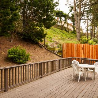 A tranquil outdoor deck area with a table and chairs, surrounded by trees and fenced for privacy.