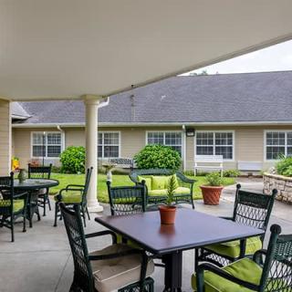 A cozy outdoor patio area with tables and chairs, surrounded by a garden and building.