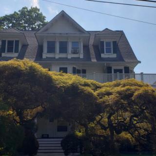 A residential house partially obscured by lush trees under a bright sky.