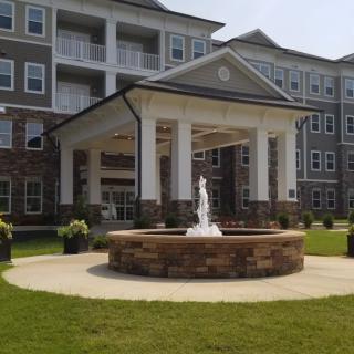 A modern building with a prominent entrance and a fountain in the front lawn.