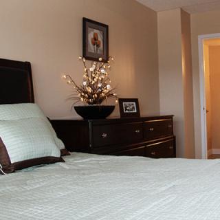 A cozy bedroom featuring a bed with soft pillows, a dresser with decorative elements, and artwork on the wall.