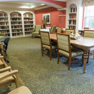 A cozy library with bookshelves, a large table, and comfortable chairs.