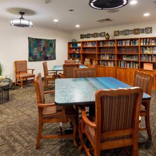 A cozy library room with wooden tables and chairs, surrounded by bookshelves.