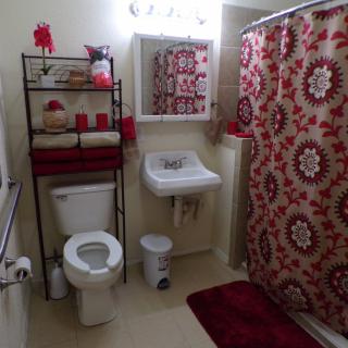A neatly organized bathroom with red and floral decor.