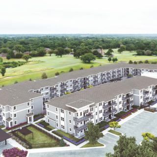 Aerial view of a suburban apartment complex with adjacent green landscape and parking area.