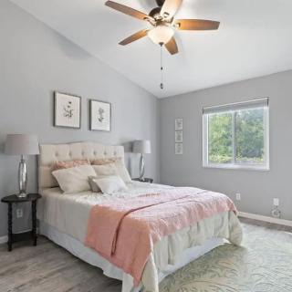 A modern bedroom with light decor, featuring a bed with pillows and a ceiling fan.